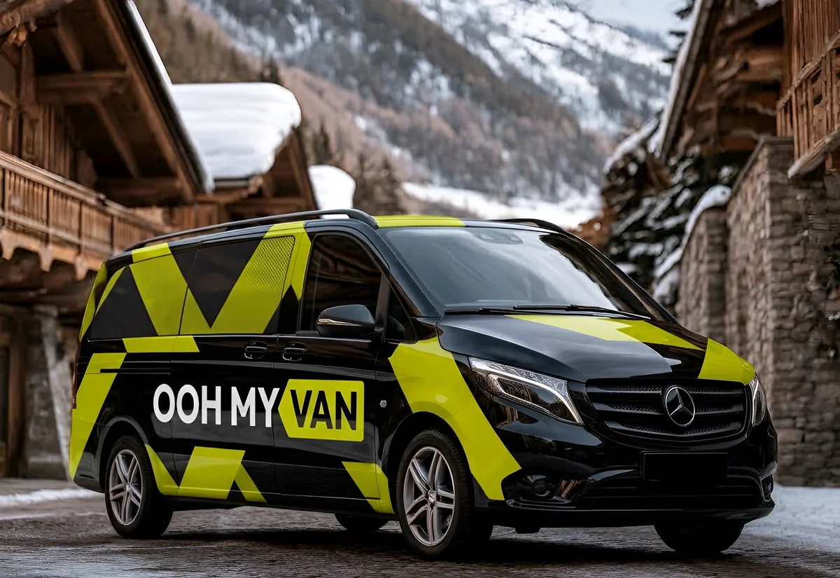 Van 9 places noir en total covering jaune-vert marqué OOH MY VAN, dans un village de montagne enneigé